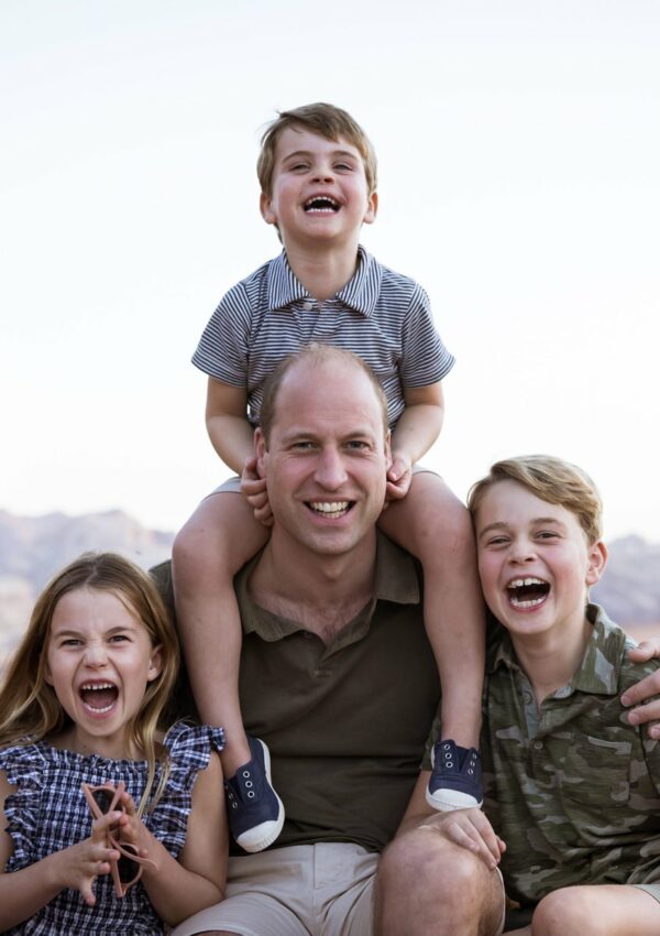 Prince William, Princess Charlotte on the left, Prince George on the right, and Prince Louis on his shoulders, are all smiling and laughing on the family's 2021 trip to Jordan